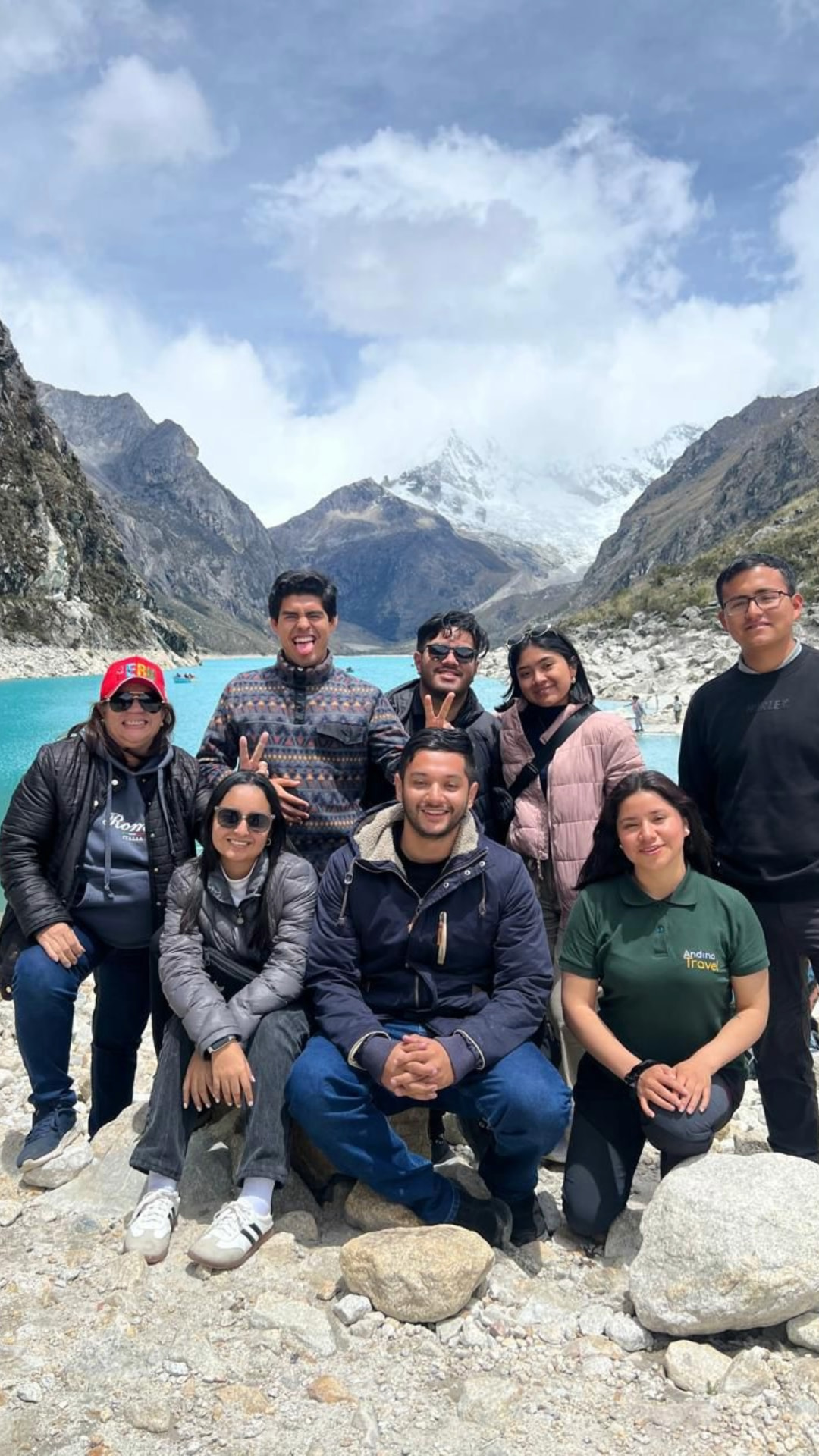 Group Experience at Paron Lagoon Group of happy travelers posing together with the turquoise Paron Lagoon and snowy peaks in the background.